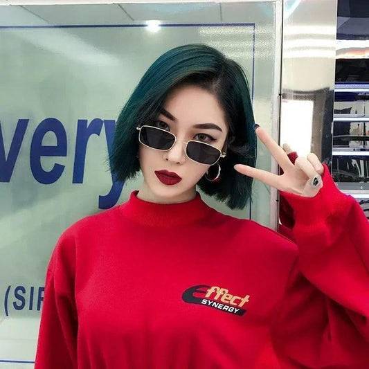 Woman wearing stylish rectangular sunglasses, red sweater, posing with peace sign in store