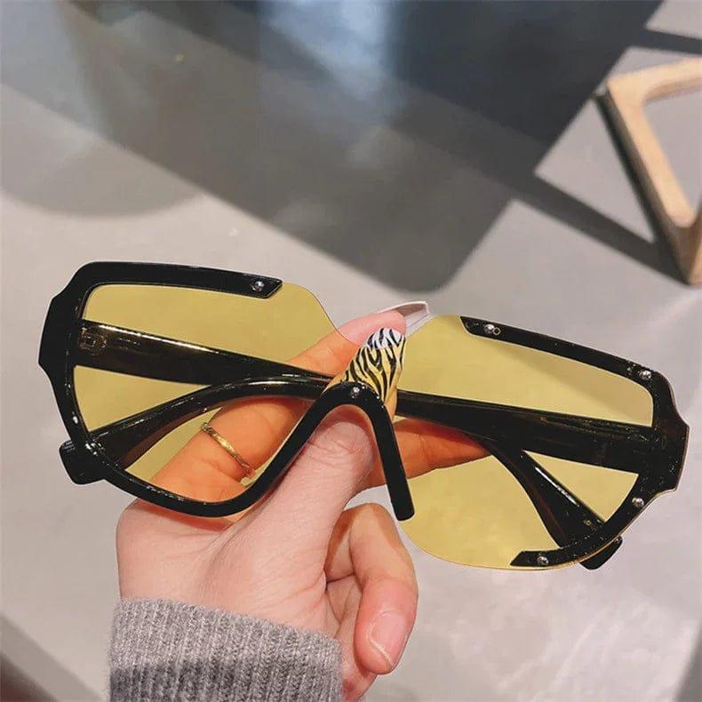 Stylish oversized sunglasses with yellow lenses and black frames, held by hand with zebra nail art.