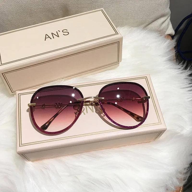 Stylish purple gradient sunglasses with glitter frame, displayed in luxury box on fluffy white surface