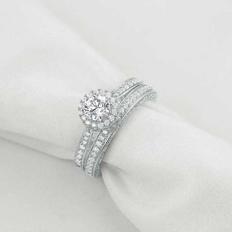 Round cut zircon engagement ring with pavé stones on silver band displayed on white fabric