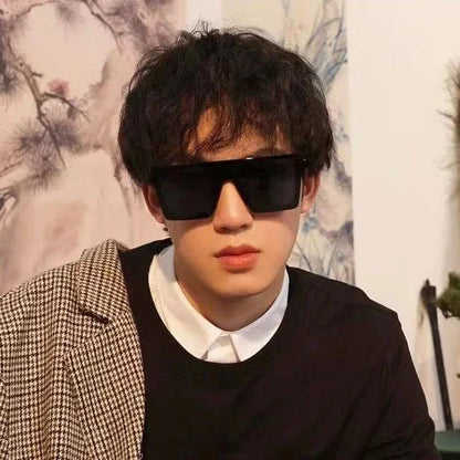 Young man with curly hair wearing oversized black sunglasses and layered outfit with checkered jacket