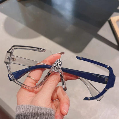Hand holding large clear shield-style glasses with blue temples and zebra print nose bridge