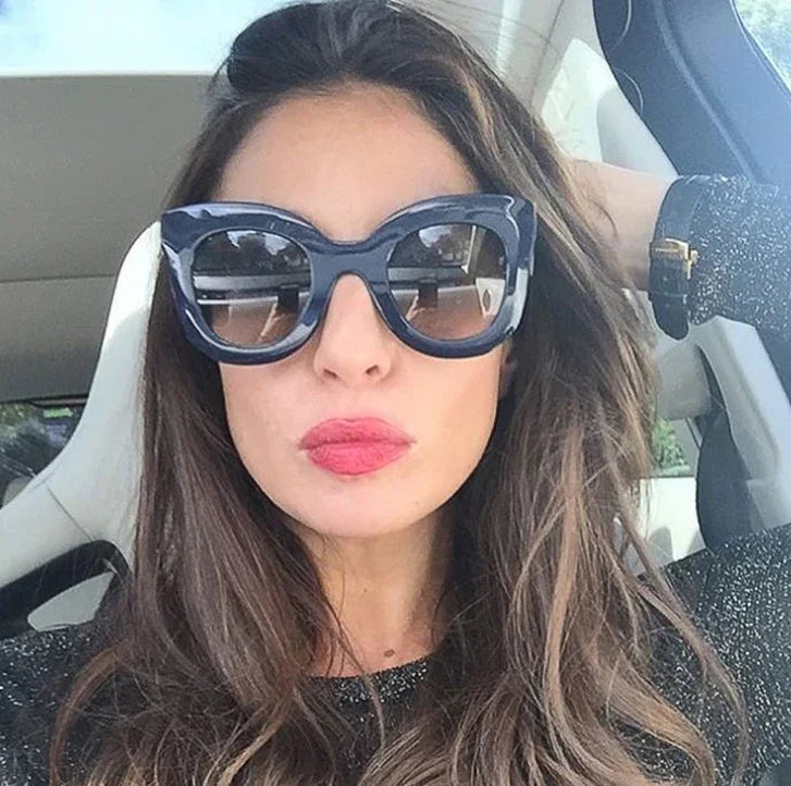 Woman with long brown hair wearing oversized black sunglasses and pink lipstick inside a car