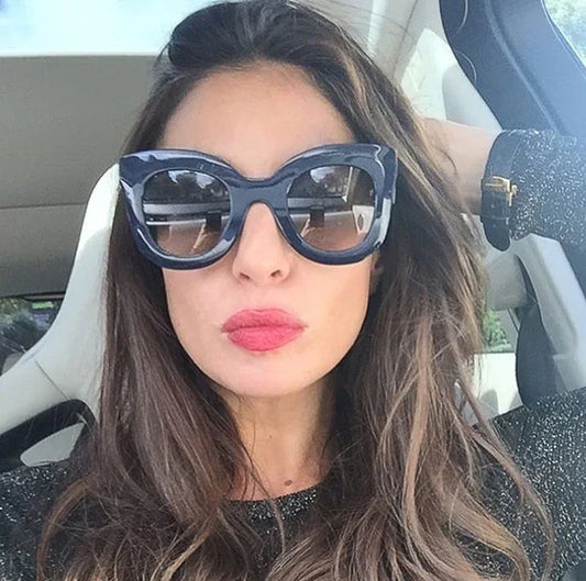 Woman with long brown hair wearing oversized black sunglasses and pink lipstick inside a car