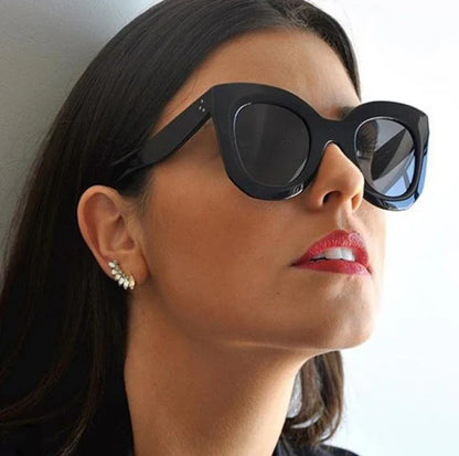 Close-up of woman wearing large black cat-eye sunglasses and red lipstick against a white background