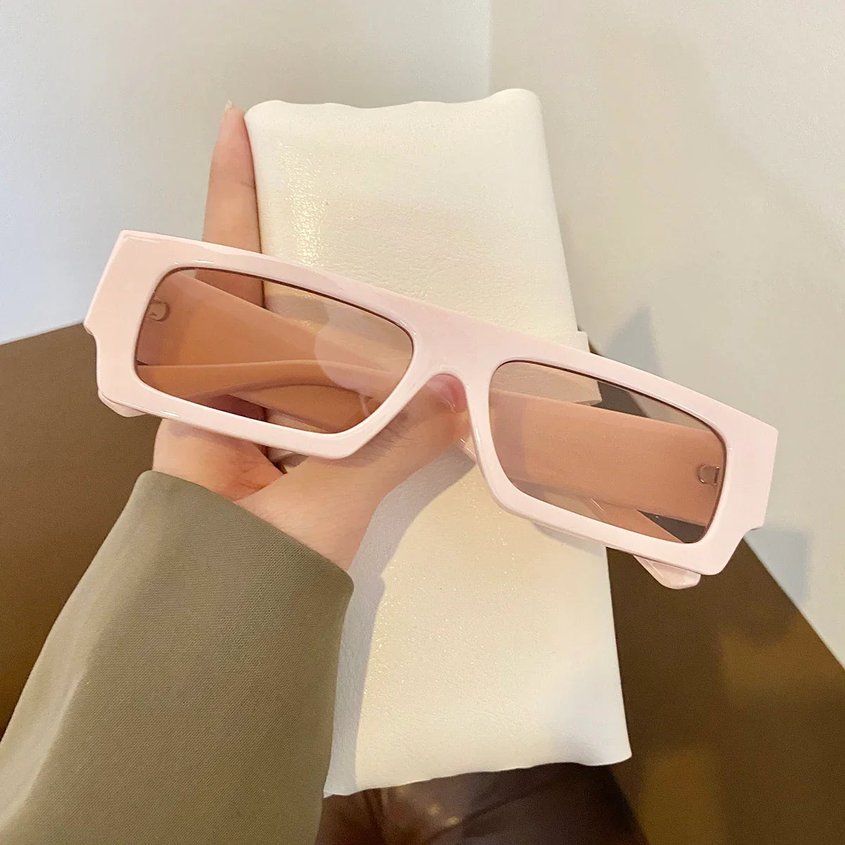 Hand holding rectangular pink sunglasses with tinted lenses and white textured case