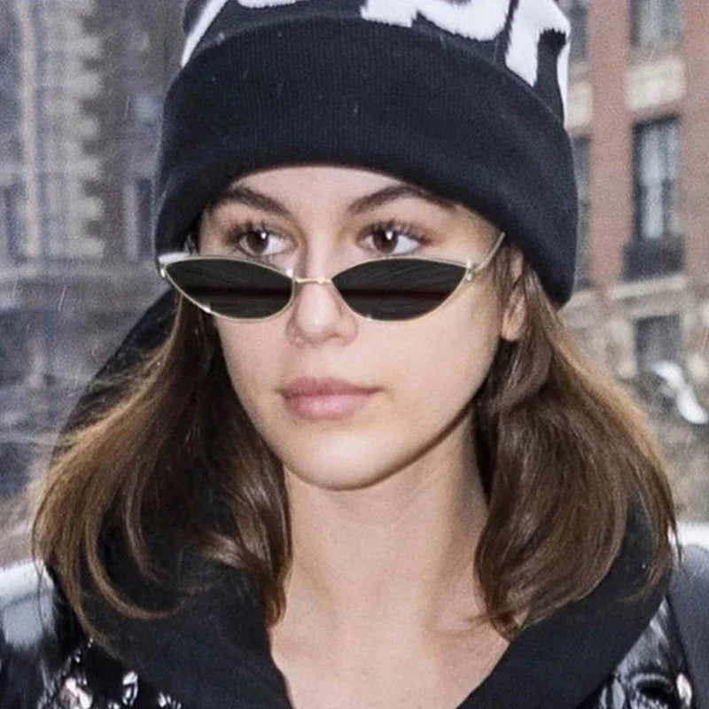 Young woman wearing black beanie and slim black sunglasses outdoors in urban setting