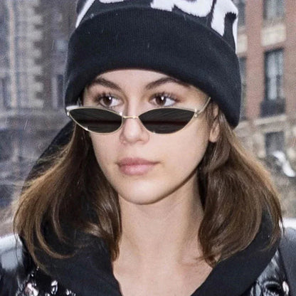 Young woman wearing black beanie and slim black sunglasses outdoors in urban setting