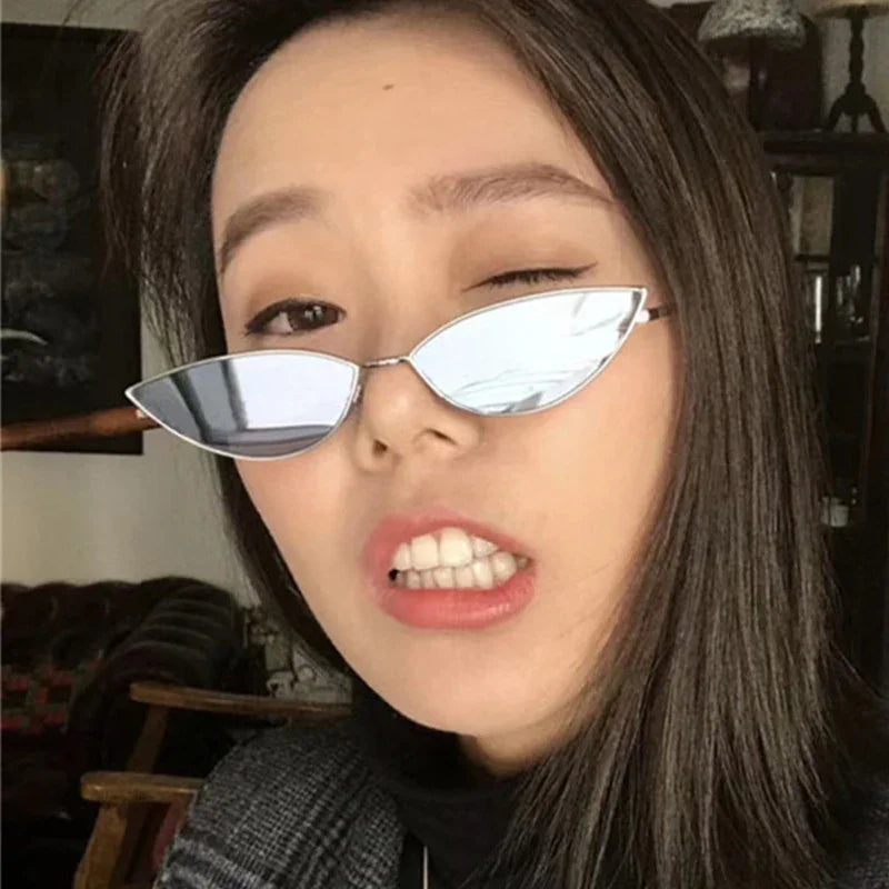 Close-up of woman winking, wearing slim silver mirrored cat-eye sunglasses and plaid jacket indoors