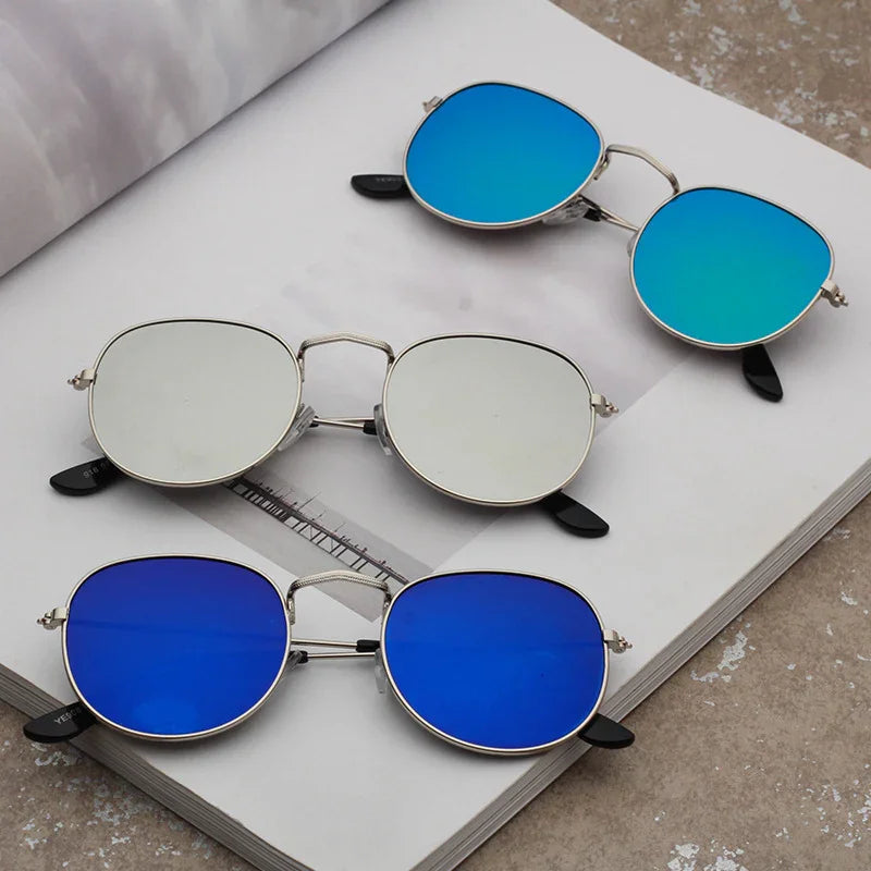 Three pairs of metal framed sunglasses with mirrored blue and silver lenses on an open book