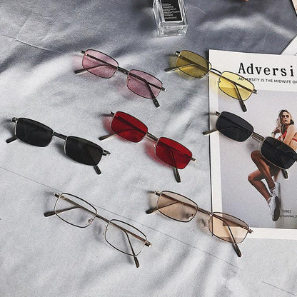 Collection of rectangular sunglasses with tinted lenses in black, red, pink, yellow, and brown on gray fabric
