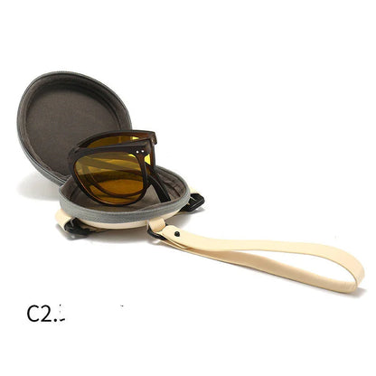 Brown sunglasses with orange lenses inside a round gray protective case with beige wrist strap on white background