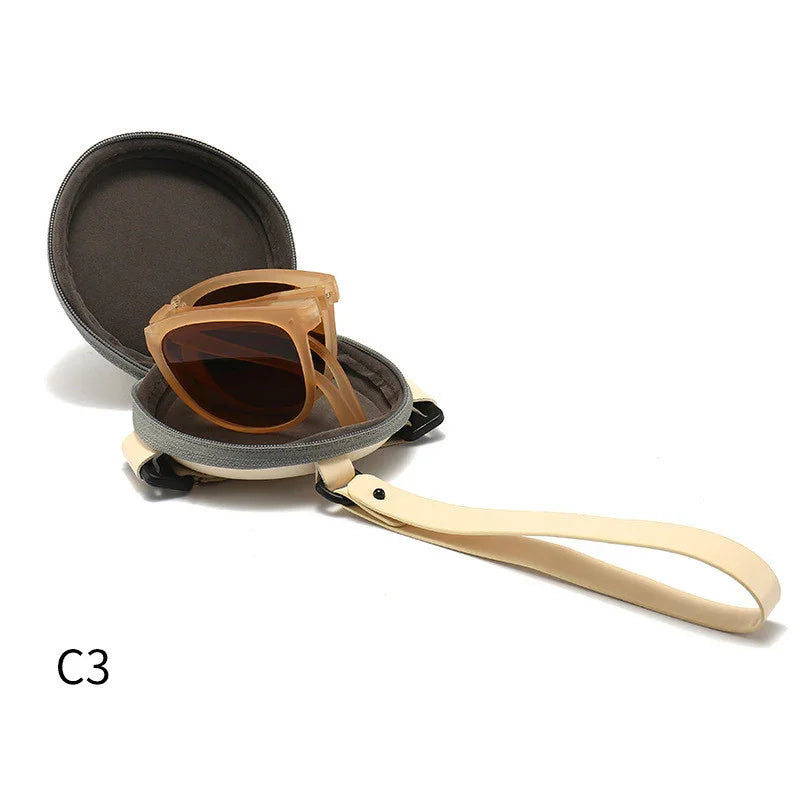 Folded translucent brown sunglasses inside round gray hard case with beige strap on white background
