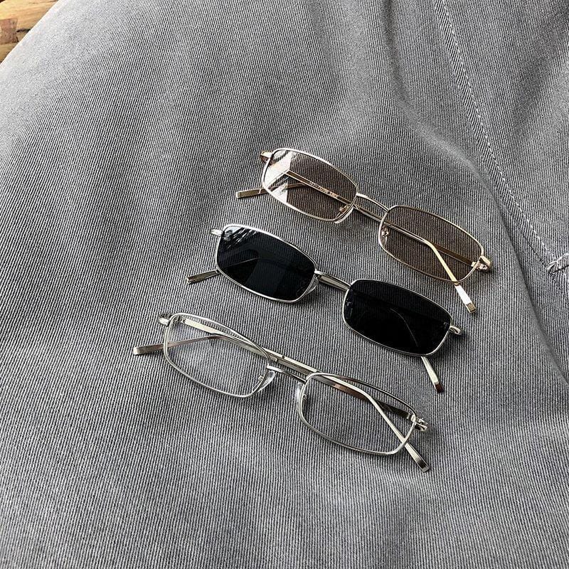 Three rectangular metal-framed eyeglasses with different lens colors on gray denim fabric