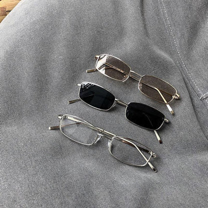 Three rectangular metal-framed eyeglasses with different lens colors on gray denim fabric