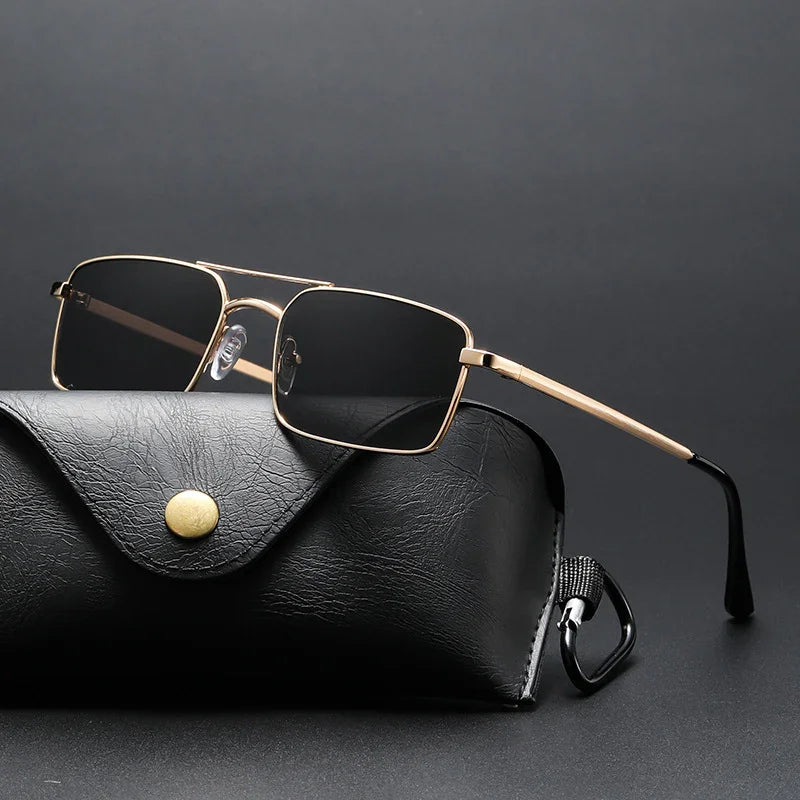 rectangular sunglasses with gold metal frame and black lenses resting on black leather case with gold button
