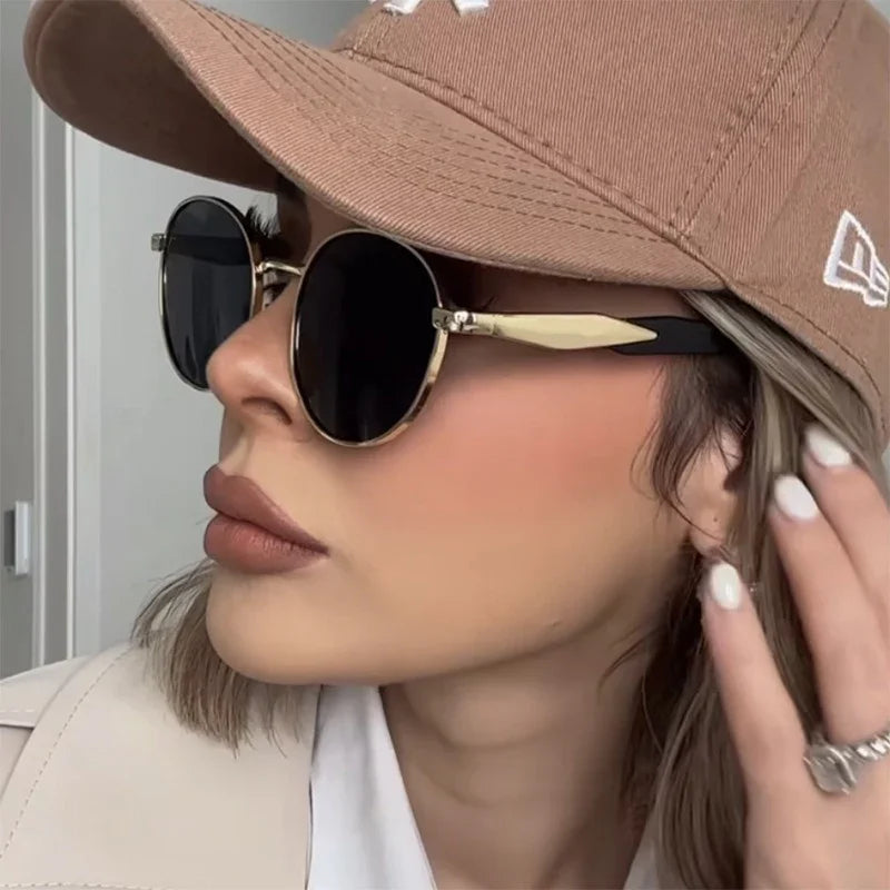 Woman wearing round black sunglasses and beige cap with light makeup and manicured nails
