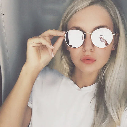 Woman with long blonde hair wearing reflective round sunglasses and white shirt, holding frame