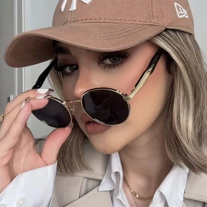 Close-up of woman wearing a beige cap, round black sunglasses, and beige blazer with white shirt