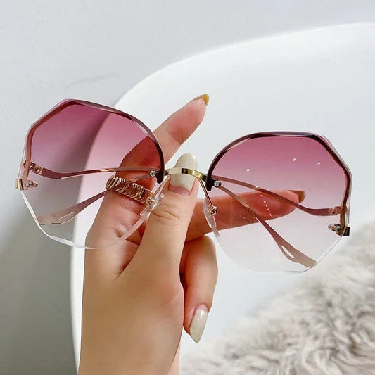 Hand holding oversized octagonal sunglasses with pink gradient lenses and gold frame