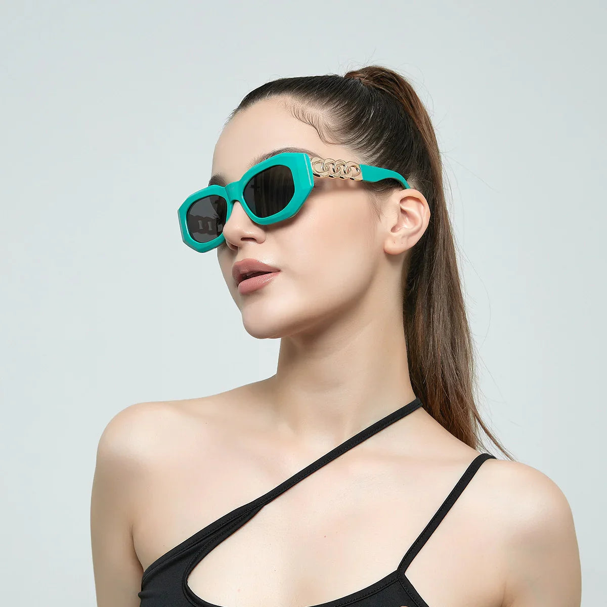 Woman wearing teal geometric sunglasses with gold chain detail and black asymmetrical top