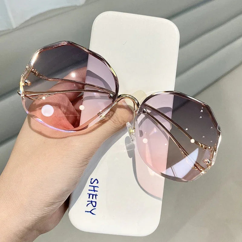 Hand holding geometric pink gradient lens sunglasses with gold metal frames on white case