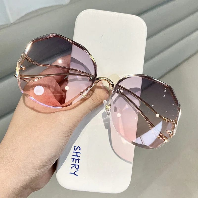 Hand holding geometric pink gradient lens sunglasses with gold metal frames on white case