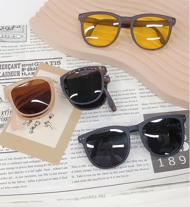Four stylish sunglasses with yellow, brown, tortoiseshell, and black lenses on newspaper and wooden surface