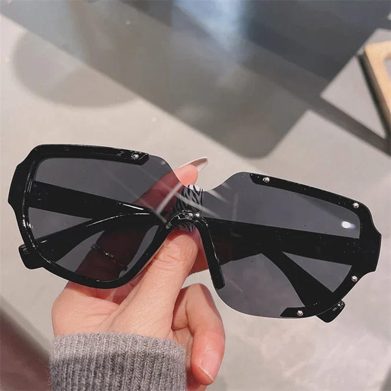Hand holding large black oversized sunglasses with angular frame and dark lenses
