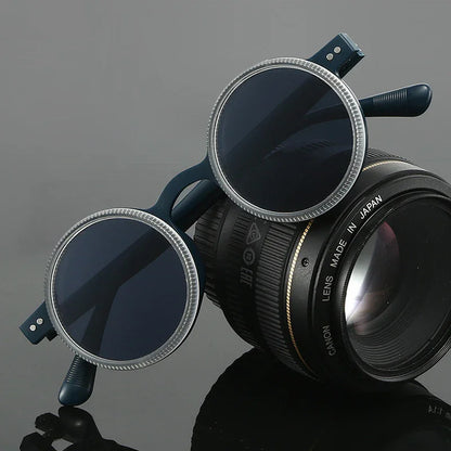 Round black sunglasses resting on a professional camera lens on a reflective surface