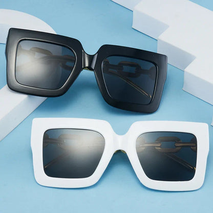 Pair of oversized square sunglasses with black and white frames on a blue surface