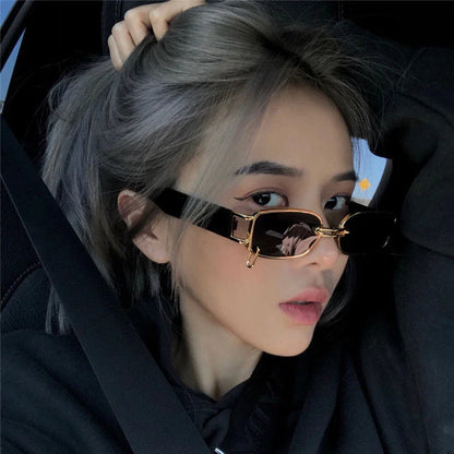 Young woman with ash gray hair wearing black and gold rectangular sunglasses inside a car