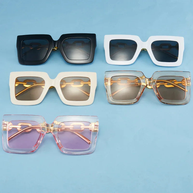 Five pairs of oversized square sunglasses in black, white, cream, brown, and pink frames on blue background