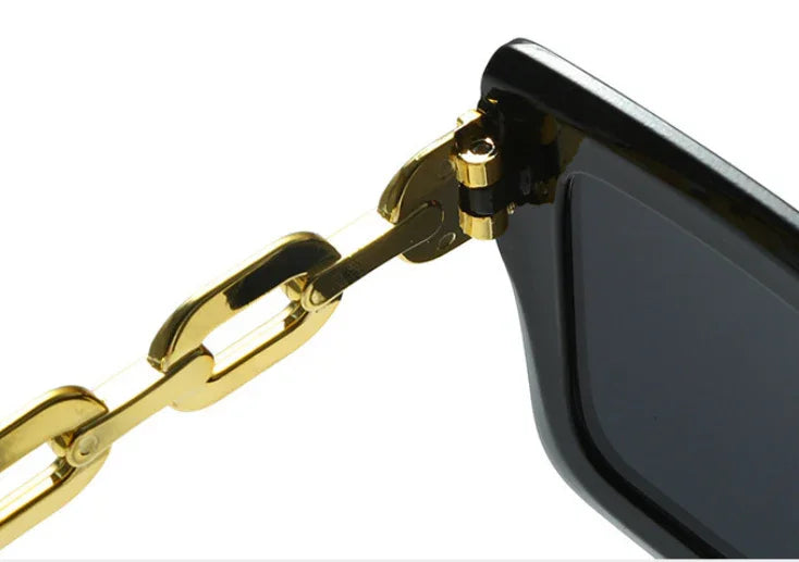 Close-up of black sunglasses with gold chain-link temple detail on white background
