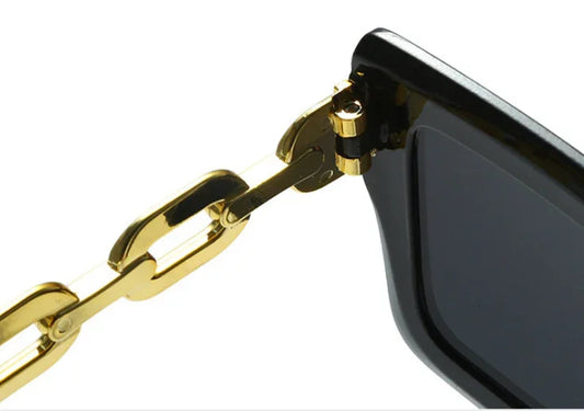 Close-up of black sunglasses with gold chain-link temple detail on white background
