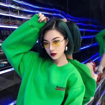 Young woman with short dark hair wearing yellow-tinted glasses and a bright green sweatshirt in neon-lit room