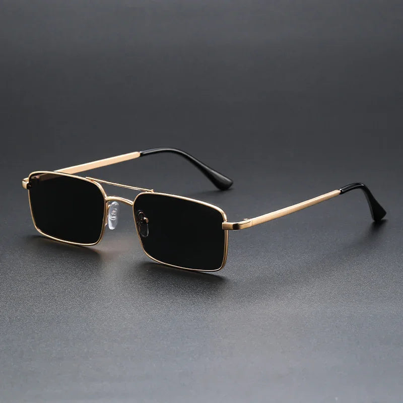 Rectangular black-lens sunglasses with gold metal frame and black temple tips on dark background