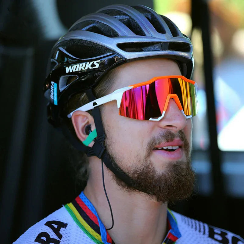 Cyclist wearing mirrored sunglasses, black helmet, rainbow-trimmed jersey outdoors