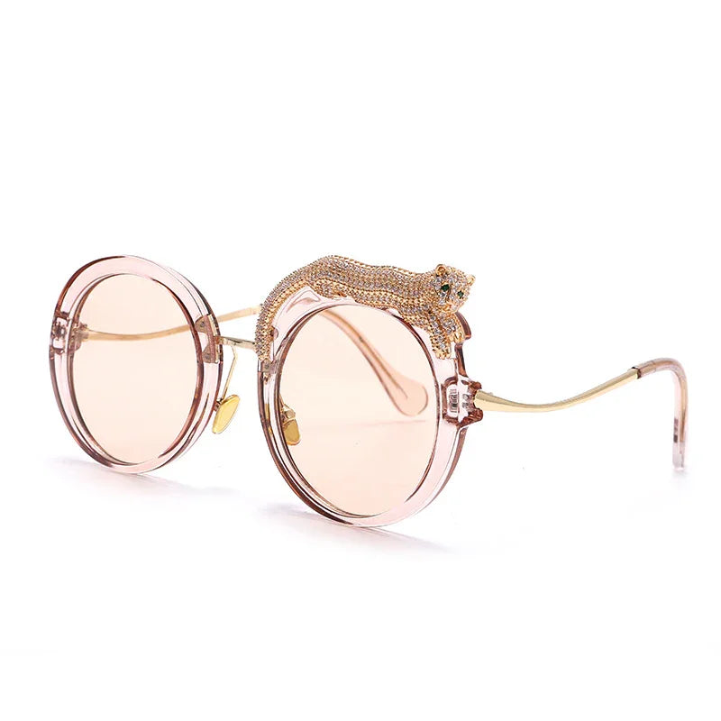 Round pink sunglasses with gold temples and a rhinestone-studded leopard detail on the frame