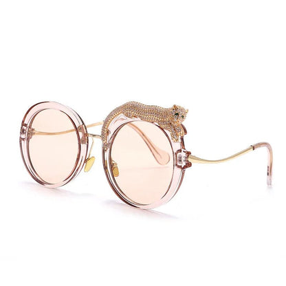 Round pink sunglasses with gold temples and a rhinestone-studded leopard detail on the frame