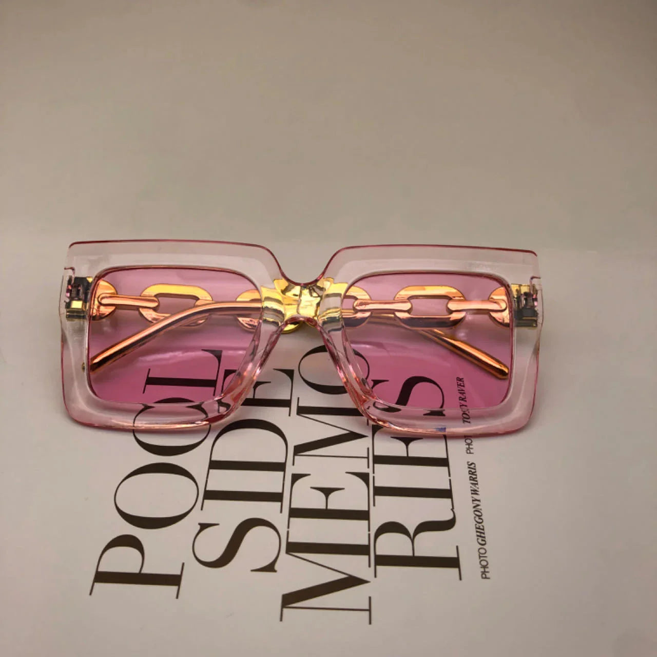 Rectangular pink-tinted fashion sunglasses with clear frames and gold chain detail on text background