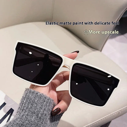 Hand holding oversized square white-frame black lens sunglasses on beige background