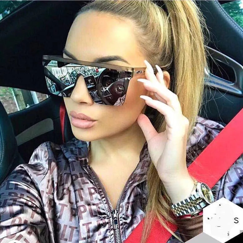 Woman wearing oversized square black mirrored sunglasses and satin monogram jacket inside car with red seatbelt