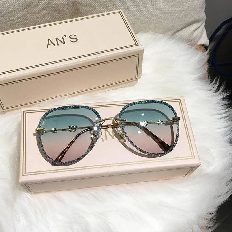 Luxury women's sunglasses with gradient blue to pink lenses and glittery blue frames on beige box