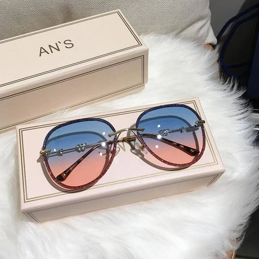 Luxury women's sunglasses with blue to pink gradient lenses and glittery frames on a beige box