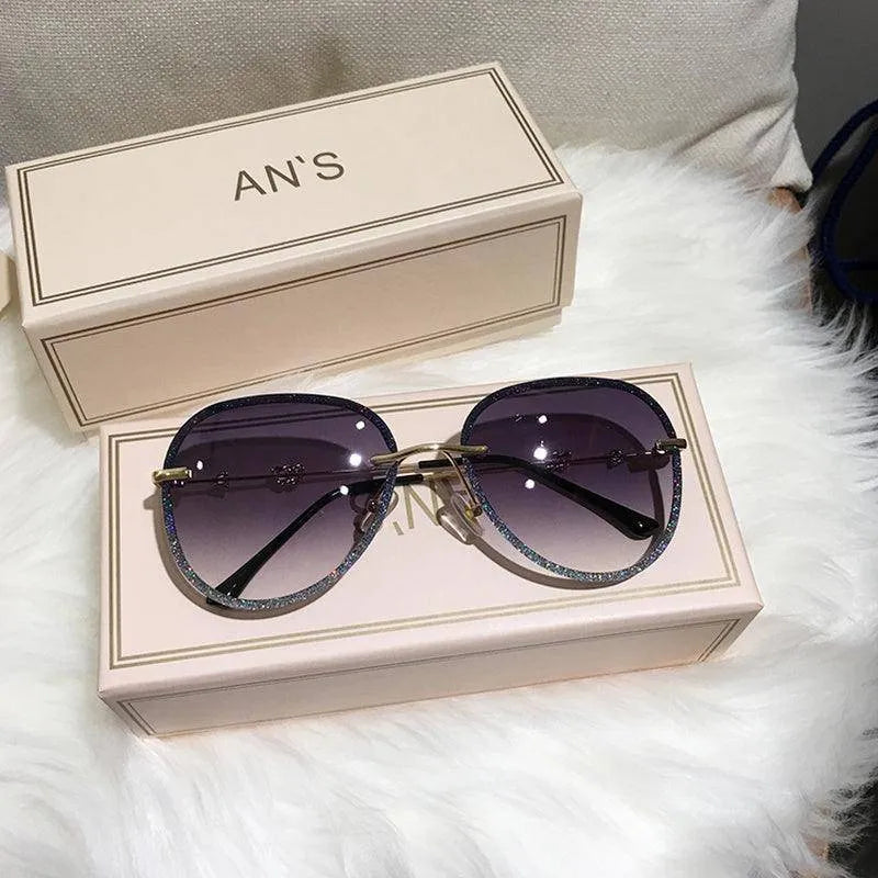 Luxury women's oversized sunglasses with gradient purple lenses and glittery frames on a beige box and soft white surface