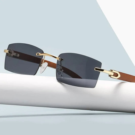 Rimless men's sunglasses with dark gray lenses, gold accents, and brown temples on a modern background.