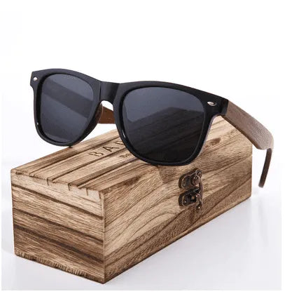 Black frame sunglasses with wooden arms and polarized dark lenses resting on a wooden box with metal latch