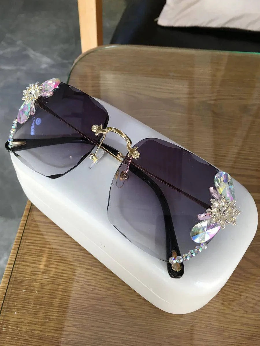 Grey frameless gradient sunglasses with rhinestone and crystal embellishments on a table