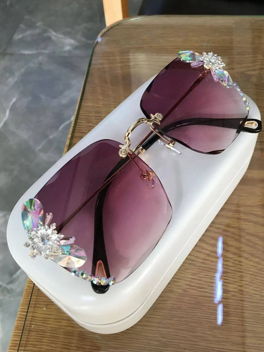 Grey frameless sunglasses with rhinestone and gradient lenses on a white case